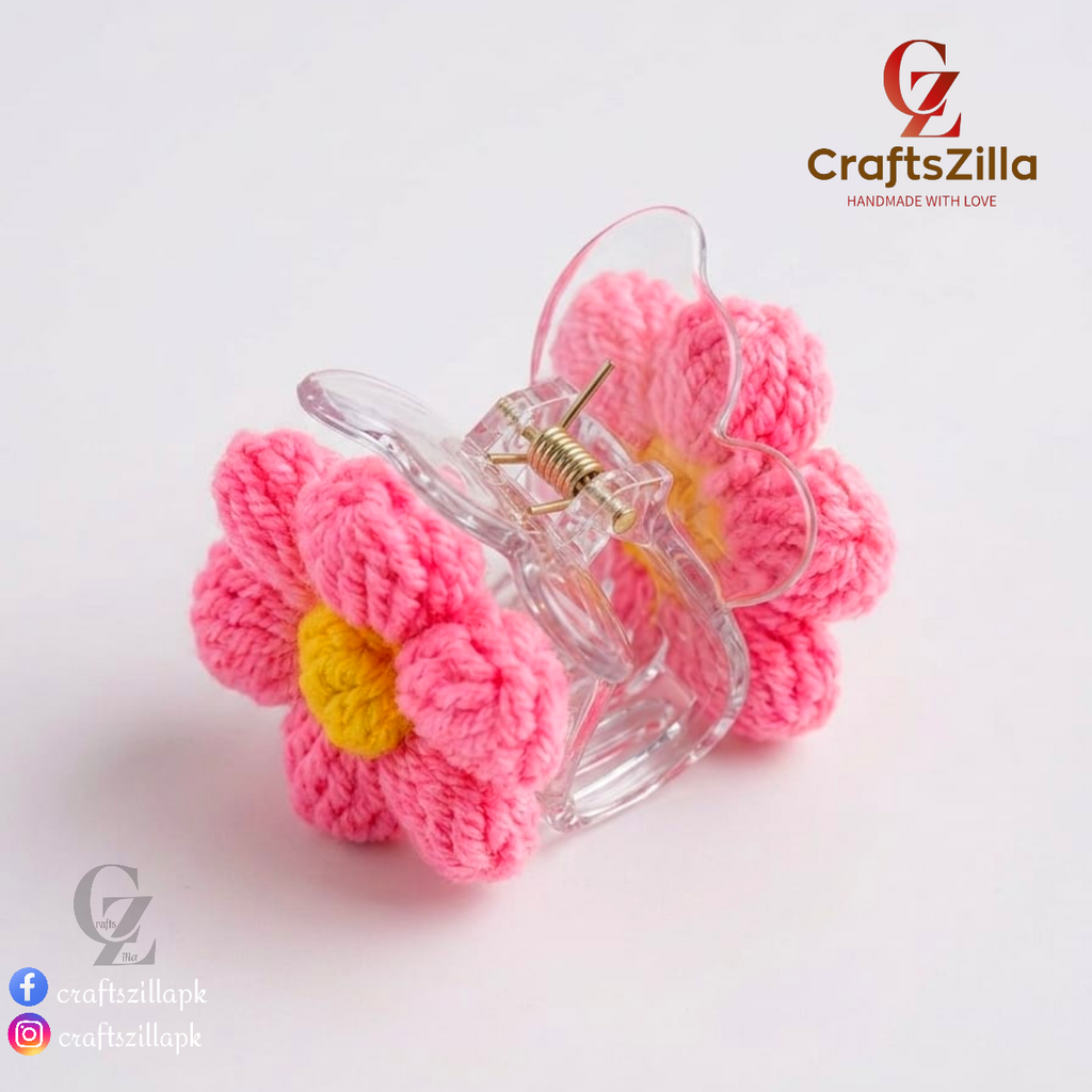 A pink crocheted flower hair claw clip with a yellow center and a clear plastic clip base, shown on a white background with CraftsZilla branding.