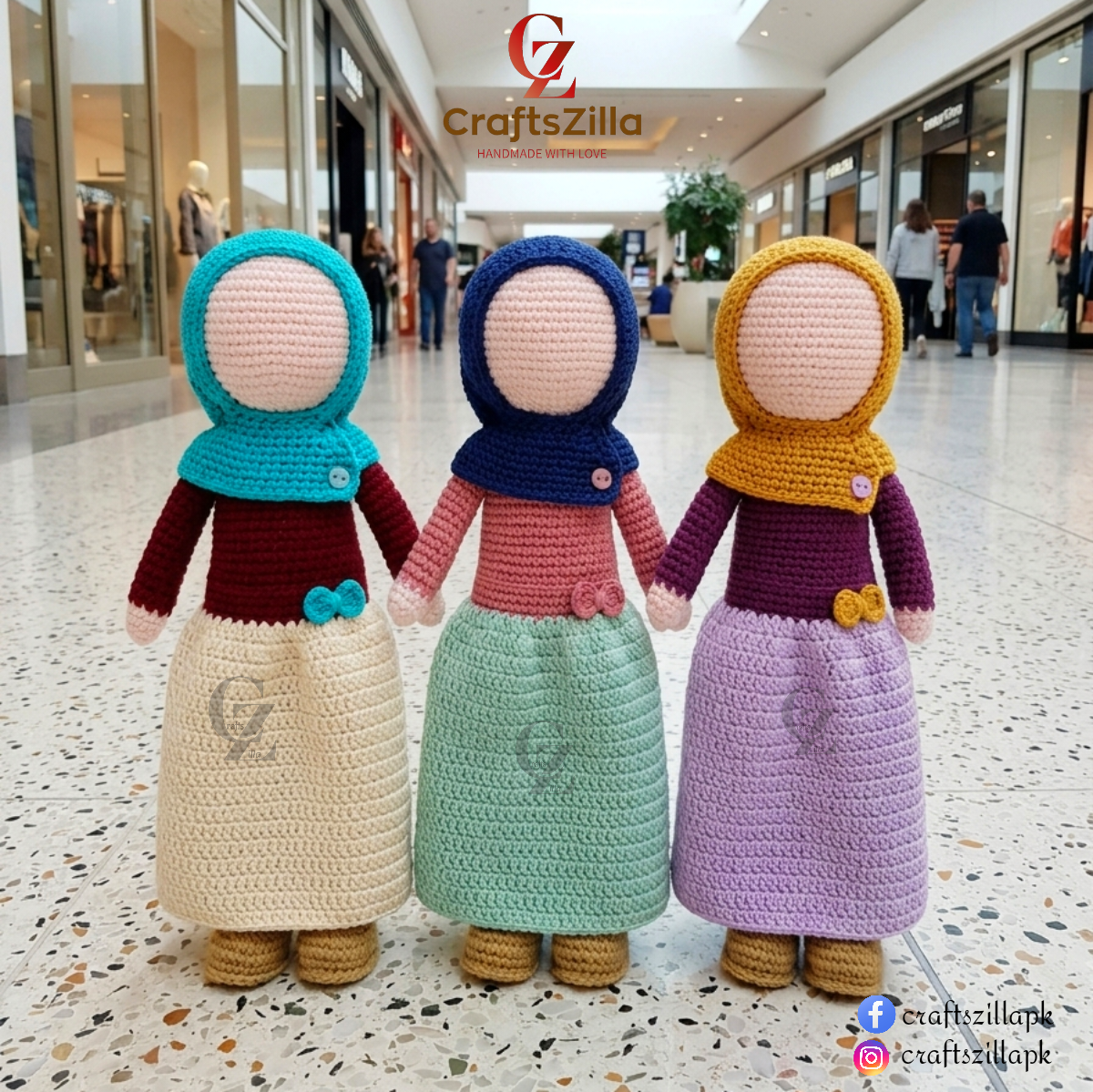 Three crocheted doll figures wearing colorful traditional headscarves and long dresses, standing side by side in a shopping mall corridor. The dolls have peach-colored faces and are dressed in teal, navy, and mustard headscarves with burgundy, pink, and purple long dresses paired with cream, mint, lavender, and yellow skirts.