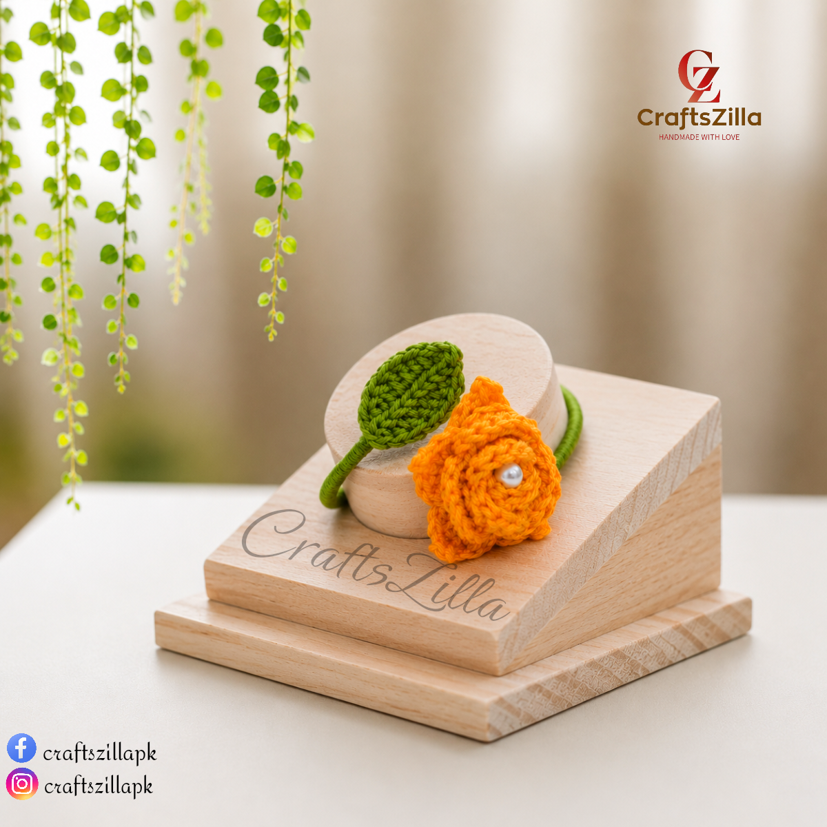 A small crocheted flower and leaf bracelet displayed on a wooden stand. The flower is bright orange with a small pearl-like center, and the leaf is green.
